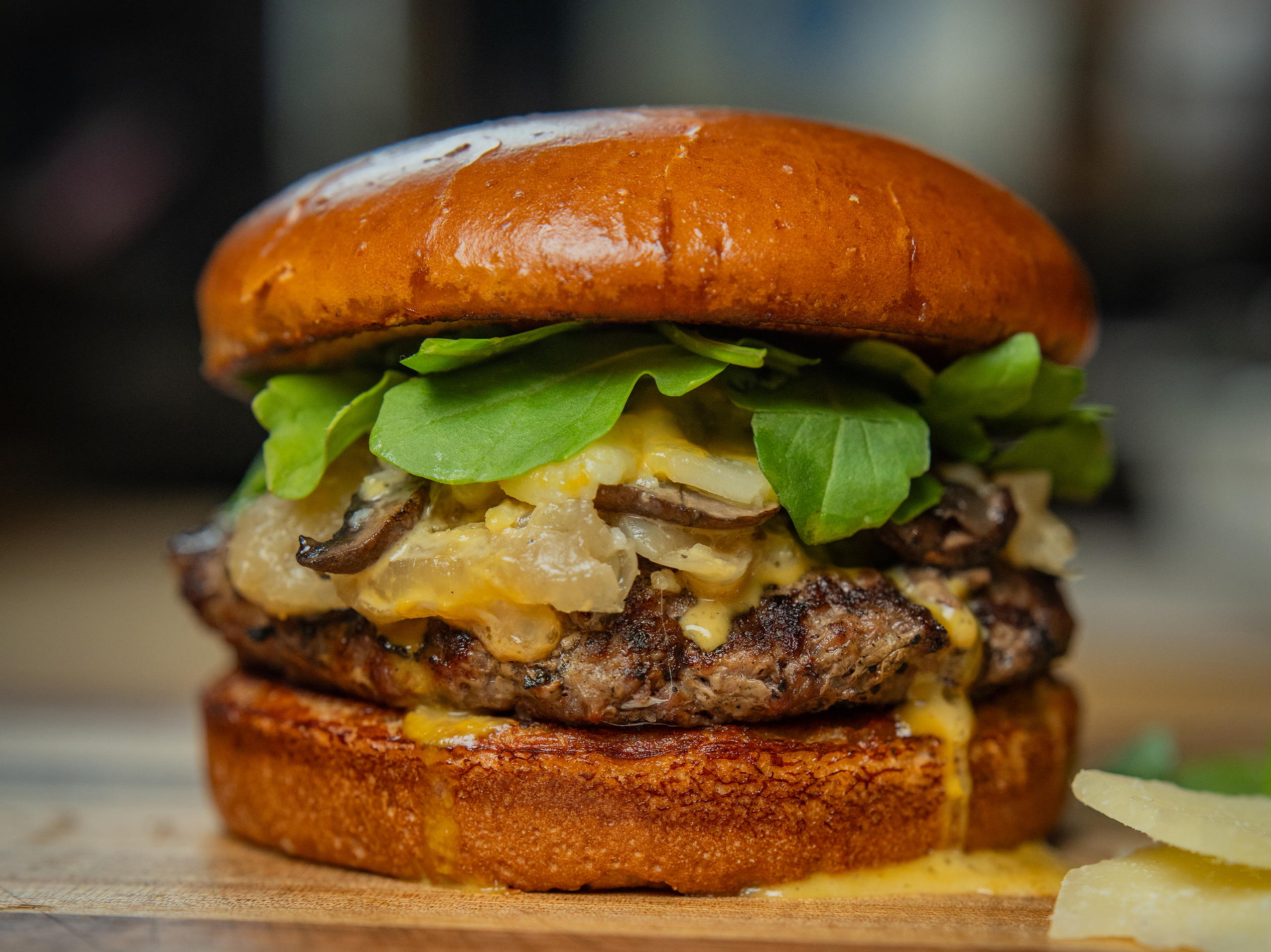 A juicy burger from True Food Kitchen featuring a thick beef patty, melted cheese, caramelized onions, fresh greens, and a glossy brioche bun, placed on a wooden surface.