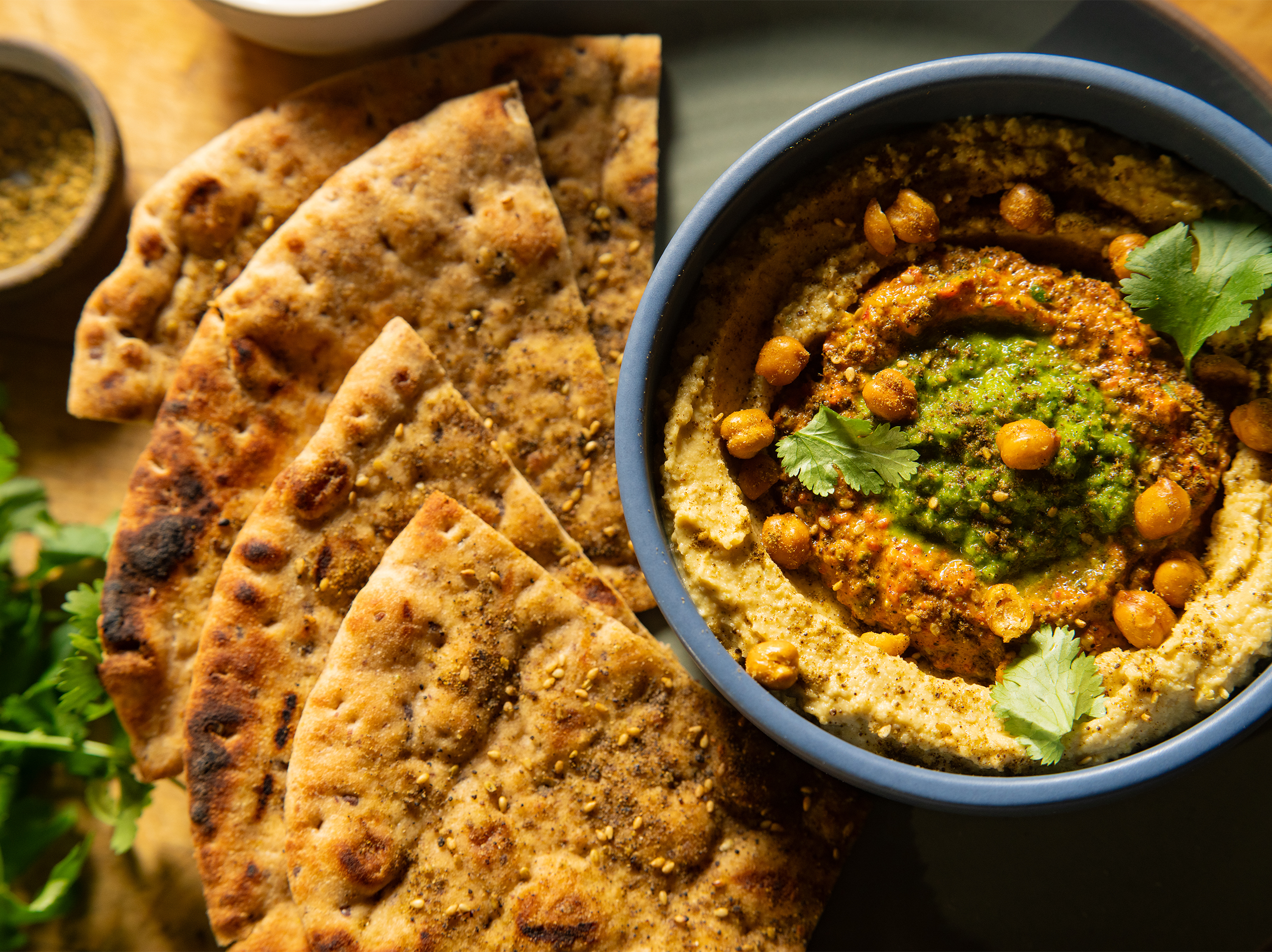 A bowl of creamy hummus topped with roasted chickpeas and herbs from True Food Kitchen, accompanied by toasted flatbread.