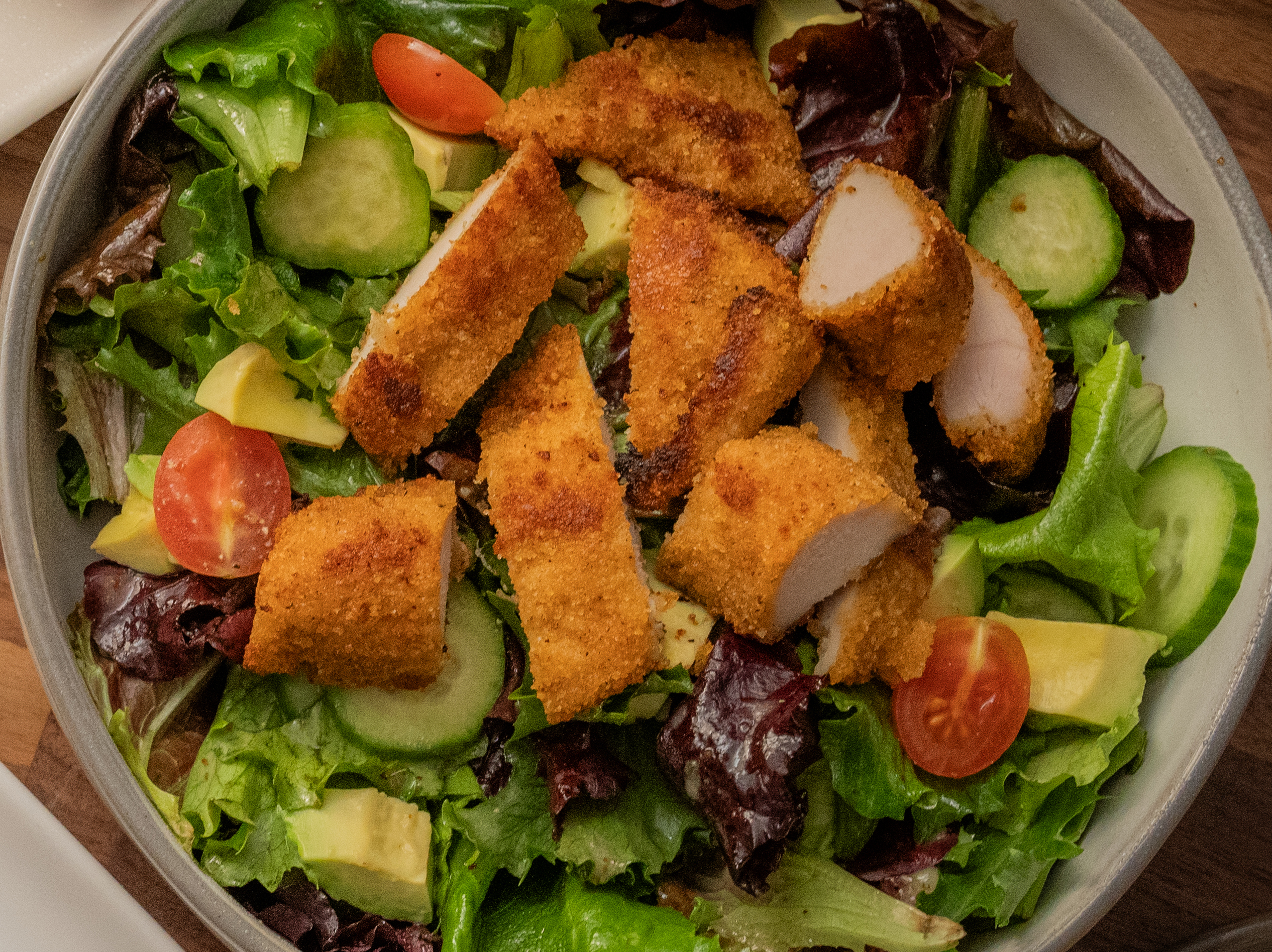 A plate of four crispy chicken tenders served with kale slaw and a dipping sauce on the side, set against an orange background.